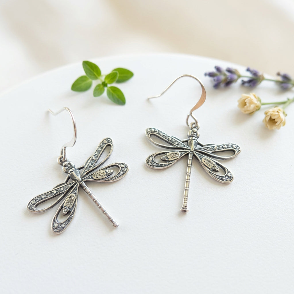 Pair of silver-plated dragonfly charm earrings with detailed openwork wings on a textured background