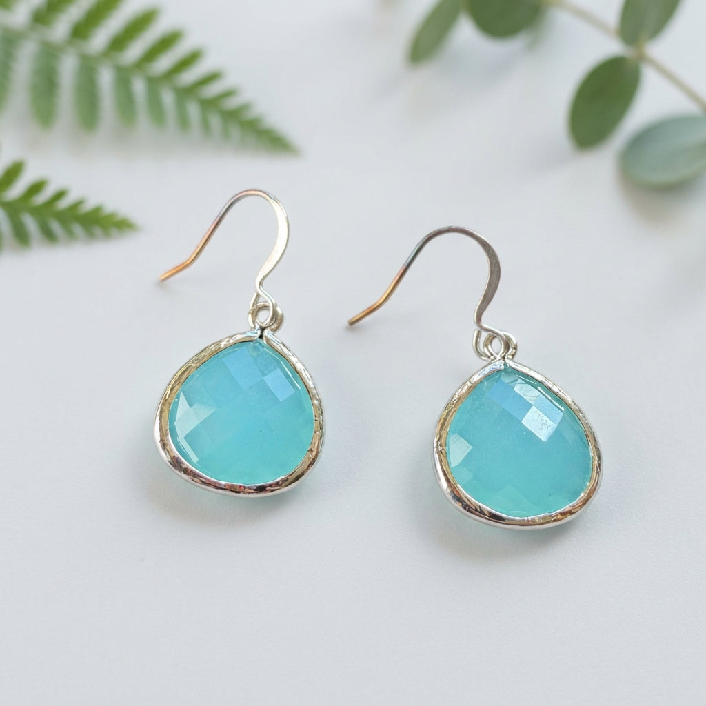 Aqua faceted teardrop earrings with silver-tone frames and curved ear wires on a textured background