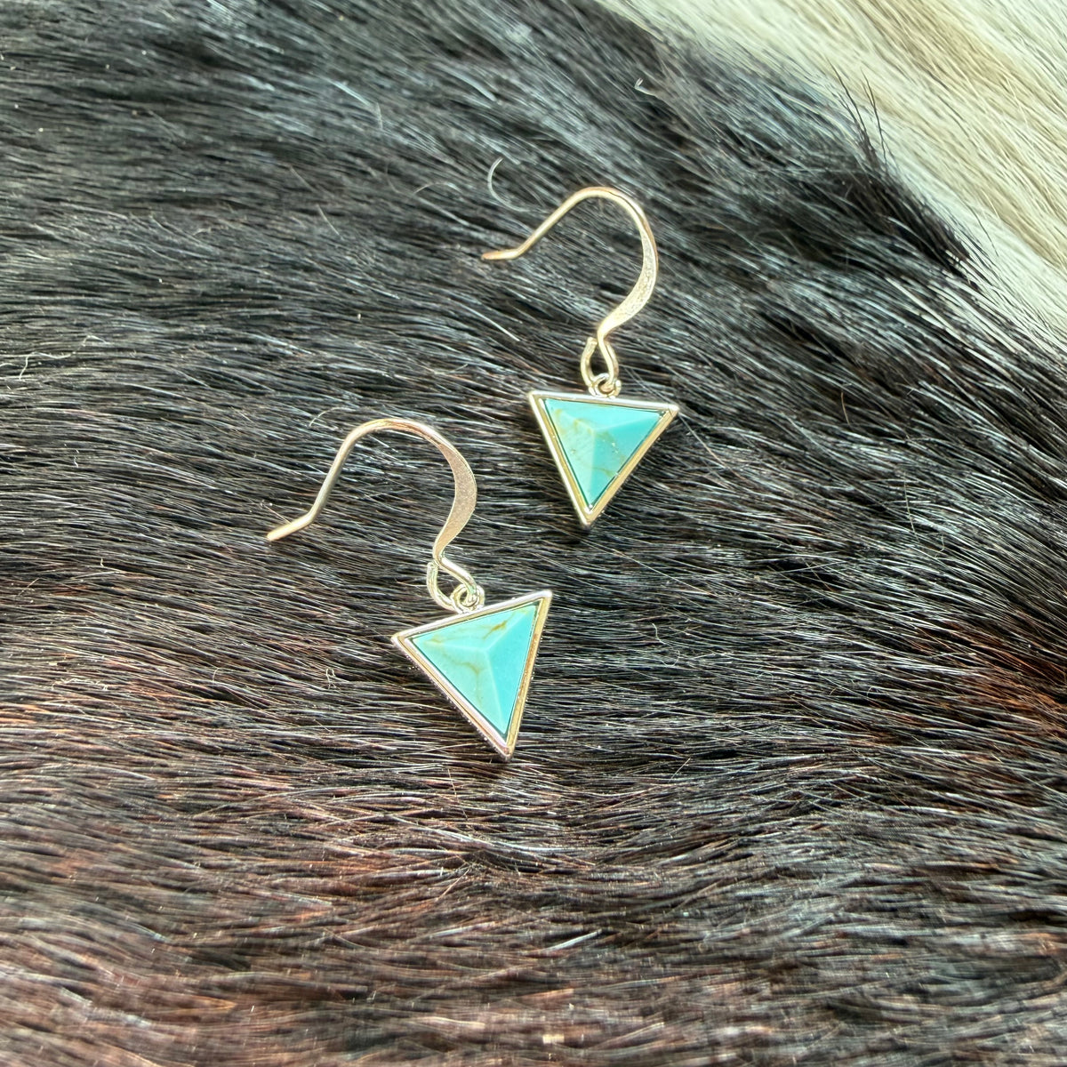 Turquoise triangle drop earrings with short curved silver-plated ear wires on a textured background