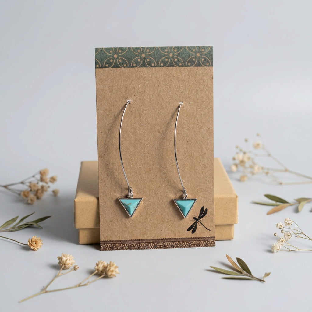 Turquoise triangle drop earrings with long curved silver-tone wires on a kraft display card
