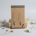 Turquoise triangle drop earrings with long curved silver-tone wires on a kraft display card